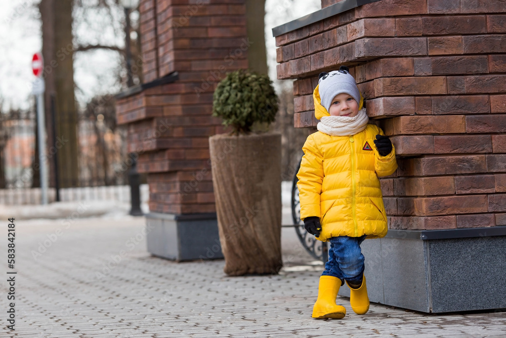 Portrait of a small child 4 years old in yellow rubber boots and a jacket. The kid walks in the park in the spring. Photo of spring and autumn holidays. Portrait of a small child 4 years old in yellow rubber boots and a jacket. The kid walks in the park in the spring. Photo of spring and autumn holidays.