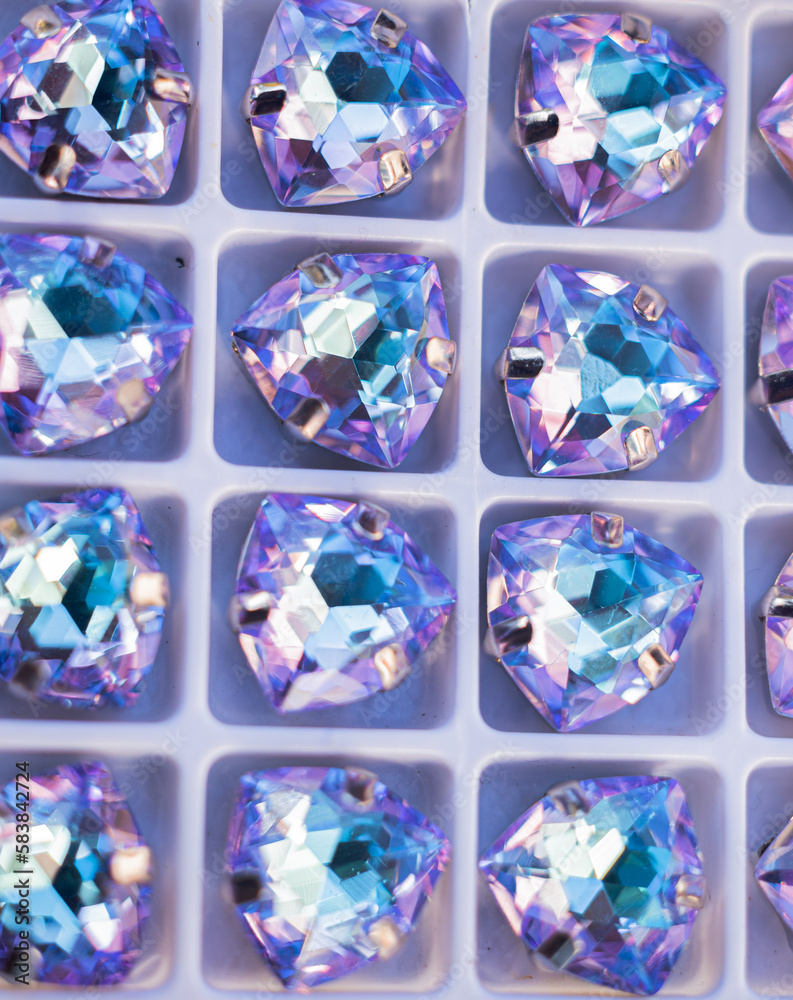 Rhinestones of various sizes and shapes are fixed in goats of gold and silver color, photographed on a wooden board of neutral color.