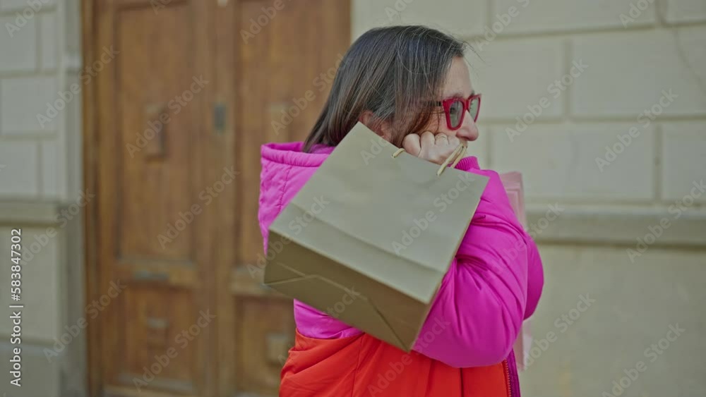 Mature hispanic woman with grey hair smiling going shopping holding bags at street