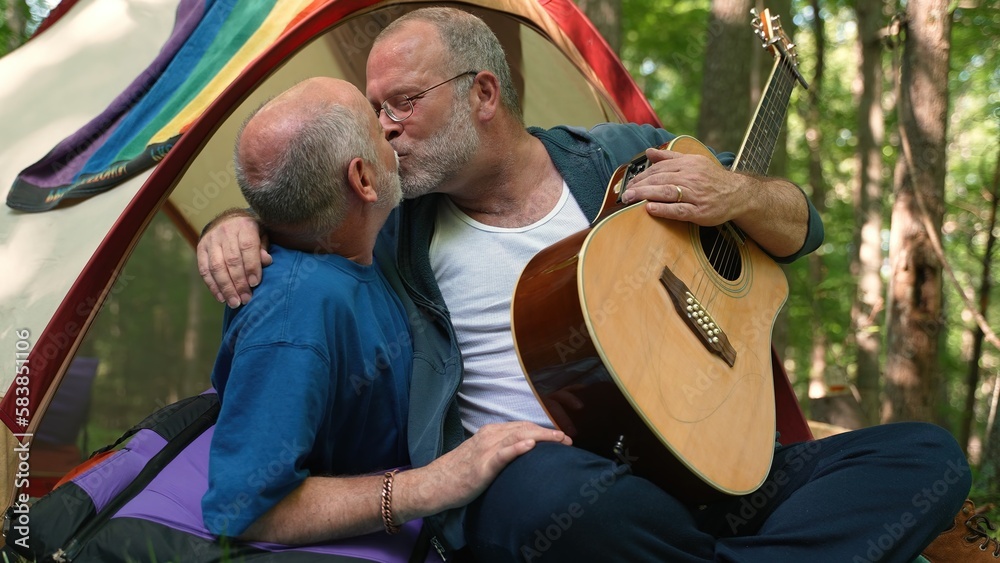 Closeup of two gay men in a tent with pride flag holding each other and kissing showing affection.