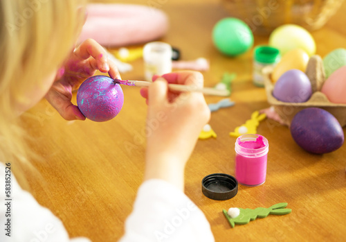 Lettle child hands painting Easter eggs on wooden table. Happy Easter. Preparation for Easter celebration. photo