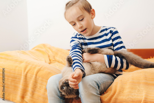 Cute boy plays with a cat at home. Happy kid hugging his cat.