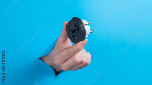 A woman is holding an outlet adapter. A woman's hand sticks out through a hole in a blue background. 