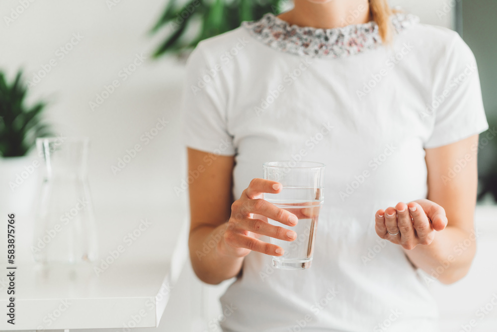 Unrecognizable woman close up holding a glass of water in one hands and vitamin pills in the palm of her other hand Unrecognizable woman close up holding a glass of water in one hands and vitamin pills in the palm of her other hand