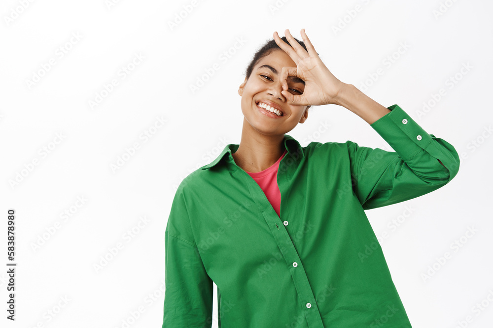 Portrait of positive young african american woman shows okay, zero gesture over eye, smiling, approve smth, recommending Portrait of positive young african american woman shows okay, zero gesture over eye, smiling, approve smth, recommending