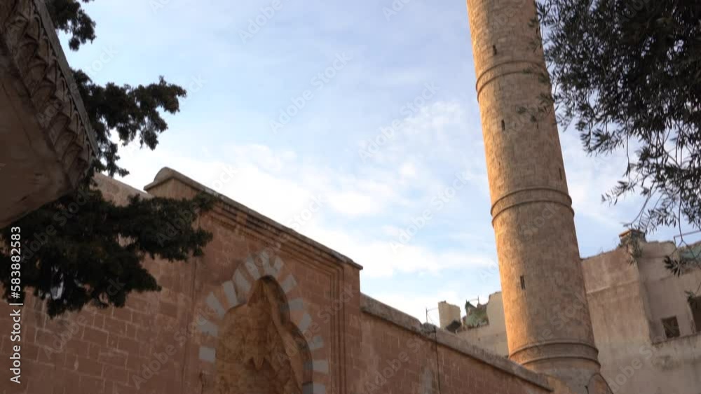 The camera tilts the grand minaret and majestic entrance gate of Latifiye Mosque in Mardin from bottom to top. We see the blue sky in the background. The camera tilts the grand minaret and majestic entrance gate of Latifiye Mosque in Mardin from bottom to top. We see the blue sky in the background.