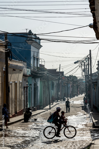 Typical backstreet under panoply of telephone wires, silhouetted family on bike, Trinidad