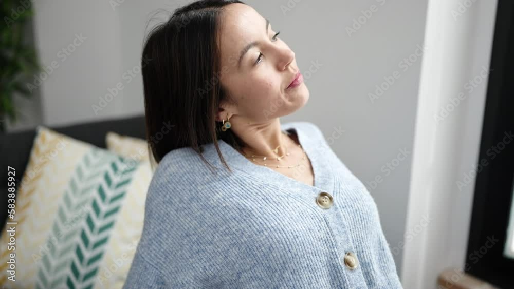 Young beautiful hispanic woman sitting on sofa stretching arms at home Young beautiful hispanic woman sitting on sofa stretching arms at home