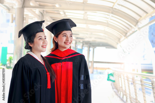 Portrait of two happy smile graduated students, young beautiful Asian women looking at same way, so proud on commencement day, celebrate successful education on graduation day for university college.