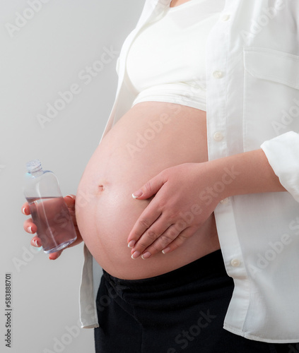 Pregnant woman applying cosmetic oil on her belly for healing stretch marks and skin elasticity photo