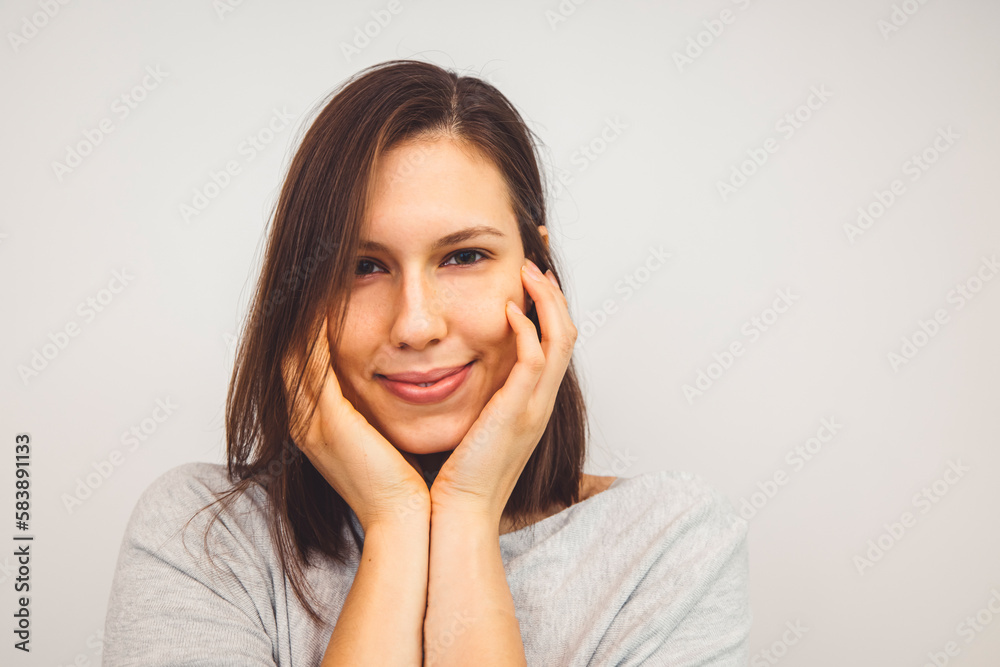 Portrait of young woman holding hands on her face with a sbtle smile looking at the camera on white background Portrait of young woman holding hands on her face with a sbtle smile looking at the camera on white background