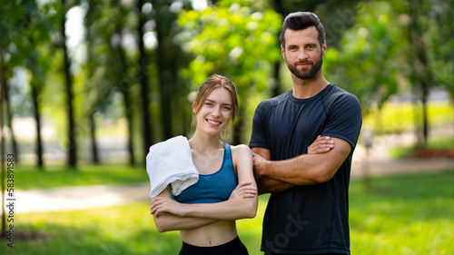 Fototapeta Naklejka Na Ścianę i Meble -  Outdoors fitness training. Portrait image of smiling young couple, woman with man or male bearded coach trainer, standing with folded hands in public park. Sport, cross fit, healthy lifestyle concept.