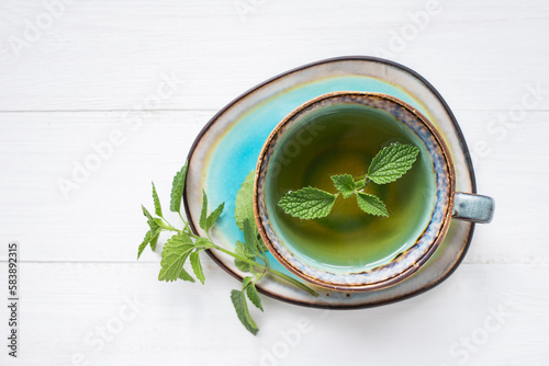 A cup of hot aromatic tea with natural fresh mint leaves on a white wooden background. Top view, space for text.