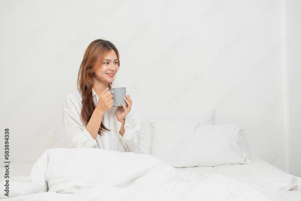 Woman in white nightgown waking up on weekend morning resting and relaxing playing with laptop mobile phone Eating bread and drinking tea in glass inside white bedroom. Morning vacation concept. Woman in white nightgown waking up on weekend morning resting and relaxing playing with laptop mobile phone Eating bread and drinking tea in glass inside white bedroom. Morning vacation concept.