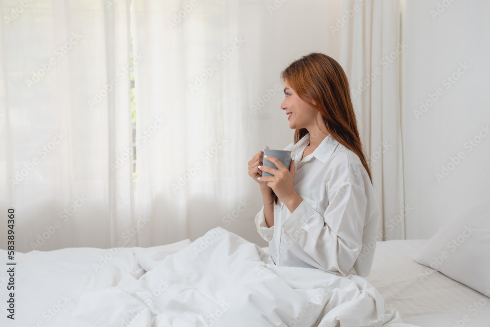 Woman in white nightgown waking up on weekend morning resting and relaxing playing with laptop mobile phone Eating bread and drinking tea in glass inside white bedroom. Morning vacation concept. Woman in white nightgown waking up on weekend morning resting and relaxing playing with laptop mobile phone Eating bread and drinking tea in glass inside white bedroom. Morning vacation concept.
