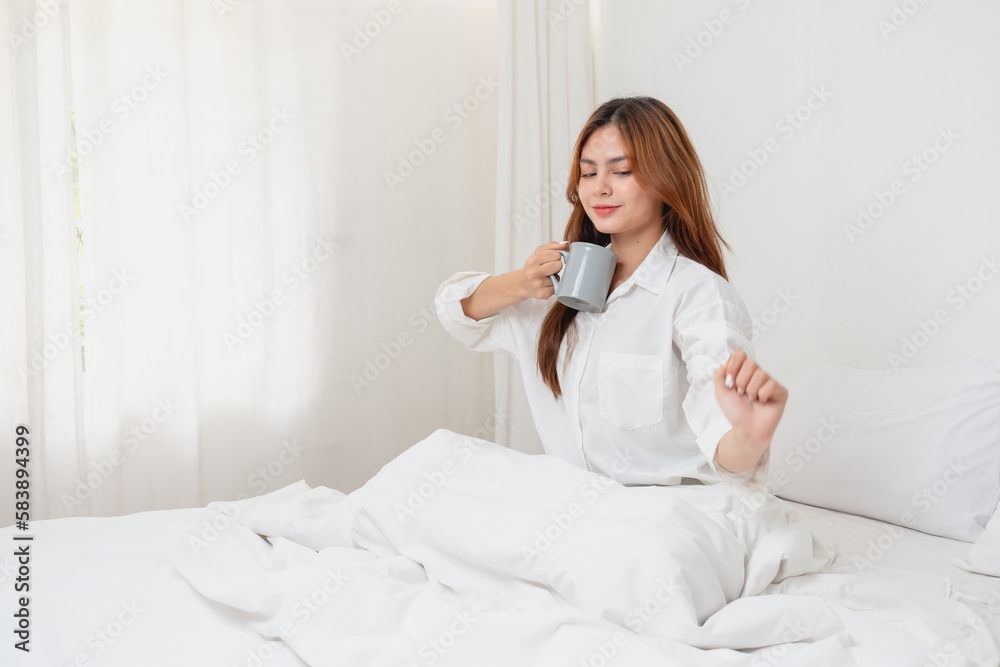 Woman in white nightgown waking up on weekend morning resting and relaxing playing with laptop mobile phone Eating bread and drinking tea in glass inside white bedroom. Morning vacation concept. Woman in white nightgown waking up on weekend morning resting and relaxing playing with laptop mobile phone Eating bread and drinking tea in glass inside white bedroom. Morning vacation concept.