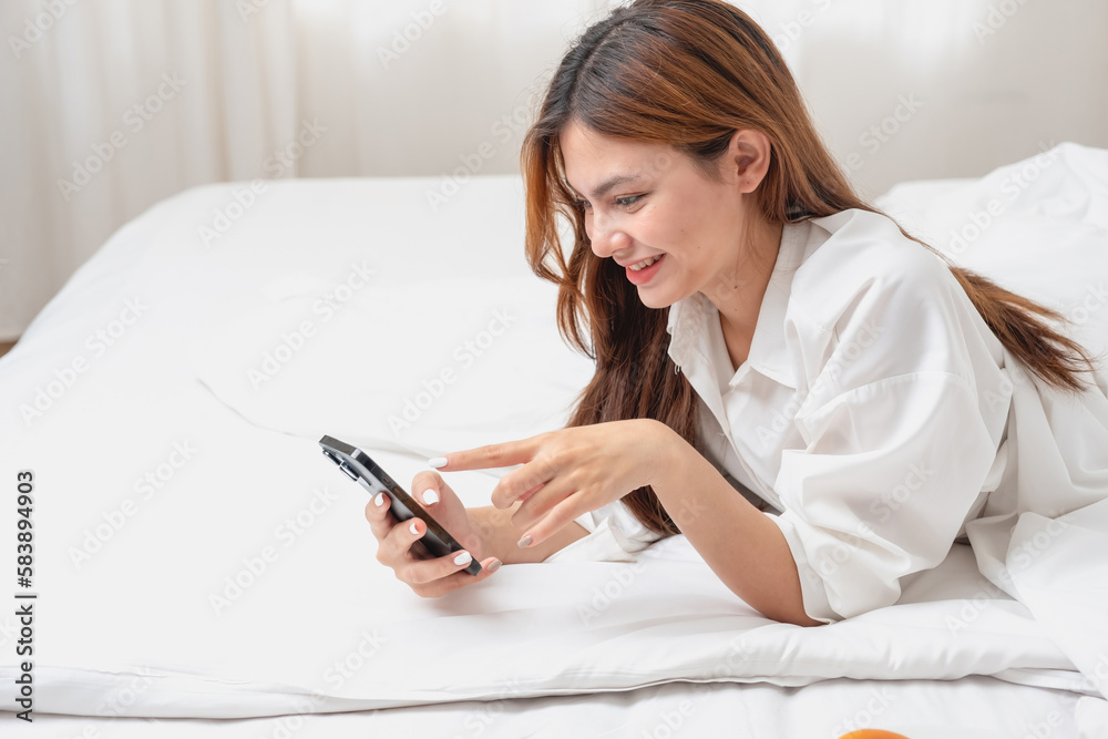 Woman in white nightgown waking up on weekend morning resting and relaxing playing with laptop mobile phone Eating bread and drinking tea in glass inside white bedroom. Morning vacation concept. Woman in white nightgown waking up on weekend morning resting and relaxing playing with laptop mobile phone Eating bread and drinking tea in glass inside white bedroom. Morning vacation concept.
