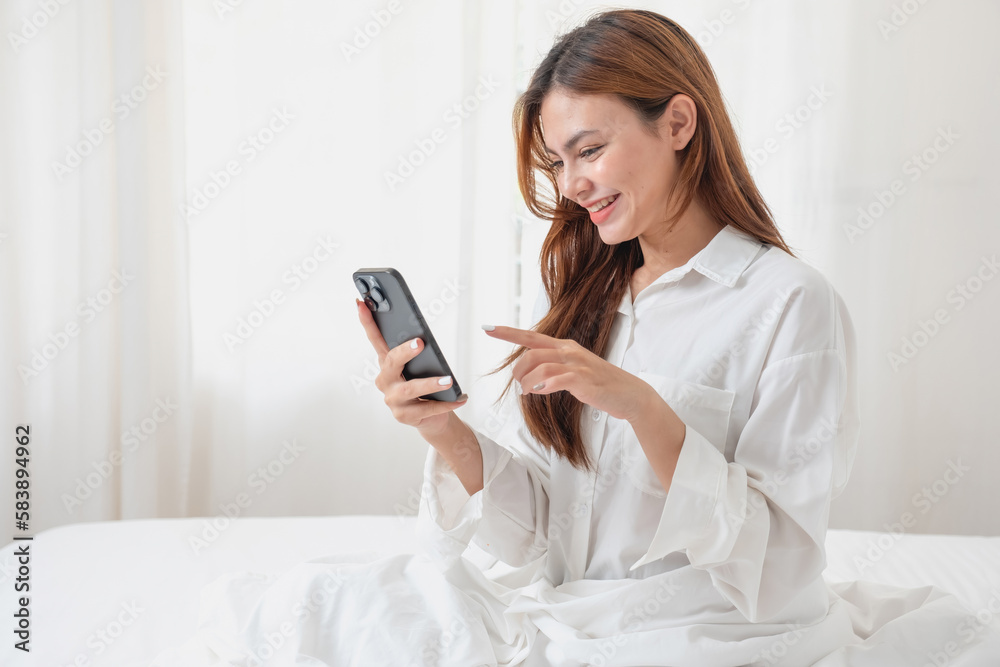 Woman in white nightgown waking up on weekend morning resting and relaxing playing with laptop mobile phone Eating bread and drinking tea in glass inside white bedroom. Morning vacation concept. Woman in white nightgown waking up on weekend morning resting and relaxing playing with laptop mobile phone Eating bread and drinking tea in glass inside white bedroom. Morning vacation concept.
