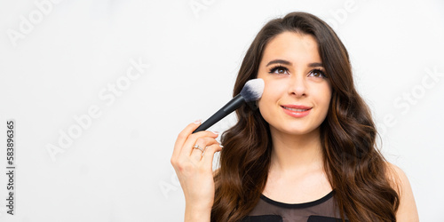 Facial Makeup. Beautiful young female putting blush or powder with a cosmetic brush on the cheek
