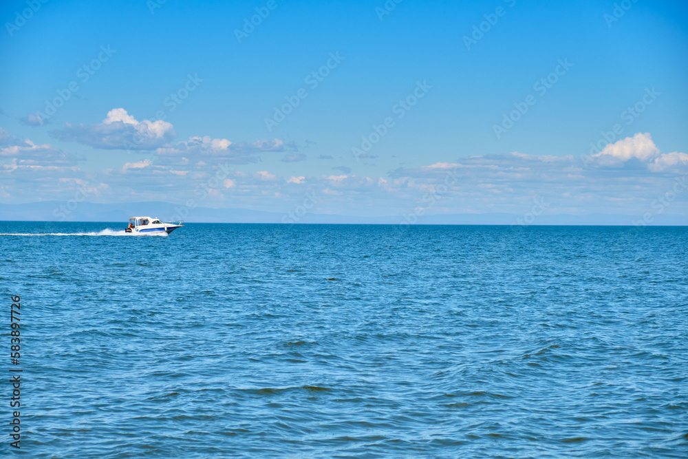 Lake Baikal coast, hill with forest, water bay. Summer travel, discovery of beauty of Earth. A boat is sailing on the lake at high speed. Siberia, Russia.
