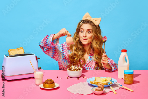 Food pop art photography. Redhead girl with bow preparing milk flakes with hungry eyes on pink tablecloth over light blue background photo