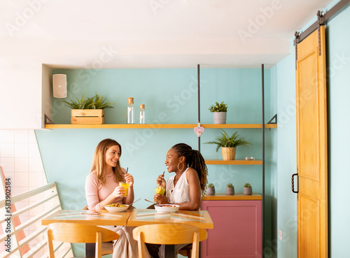 Young black and caucasian woman having good time, drinking fresh juices and having healthy breakfast in the cafe