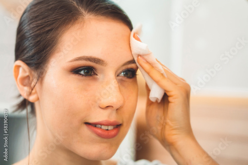 Close up woman removing make up off her face using micellar water on a cotton pad 