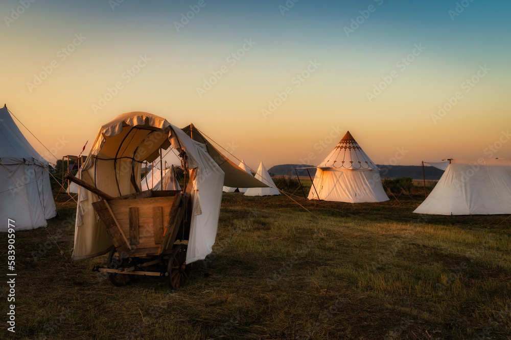 Historical reenactment of Hussars, Slavic or Vikings tribe encampment with wooden cart and tent camp from 16th century at sunrise, Gniew, Poland - obrazy, fototapety, plakaty 