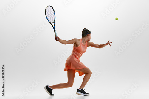 Serving ball with racket. Portrait of young woman, professional female tennis player in motion, training against white studio background. Concept of professional sport, movement, health, action. Ad