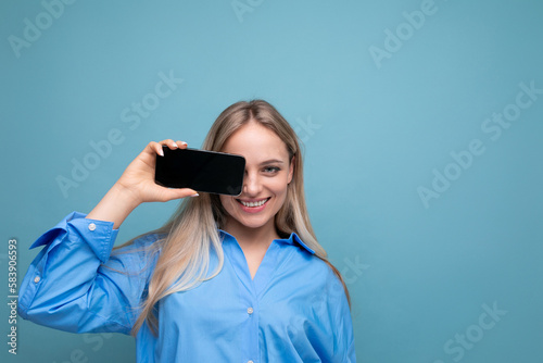 smiling attractive blond girl showing blank smartphone screen with mockup for web page on blue background