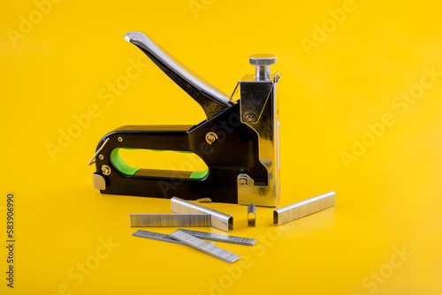Industrial and home mechanical Stapler and brad gun with a range of different types of stapels brads isolated on a yellow background