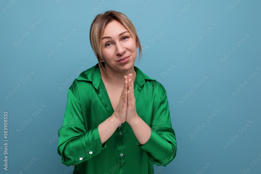 attractive blond young woman in green silk shirt praying on blue background with copy space attractive blond young woman in green silk shirt praying on blue background with copy space