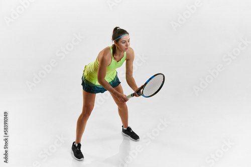 Ready to play. Athletic young woman, professional female tennis player in uniform posing with tennis racket against white studio background. Concept of professional sport, movement, health, action. Ad