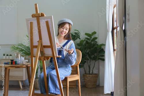 Young female artist mix color on palette to painting artwork on canvas with enjoying in home studio