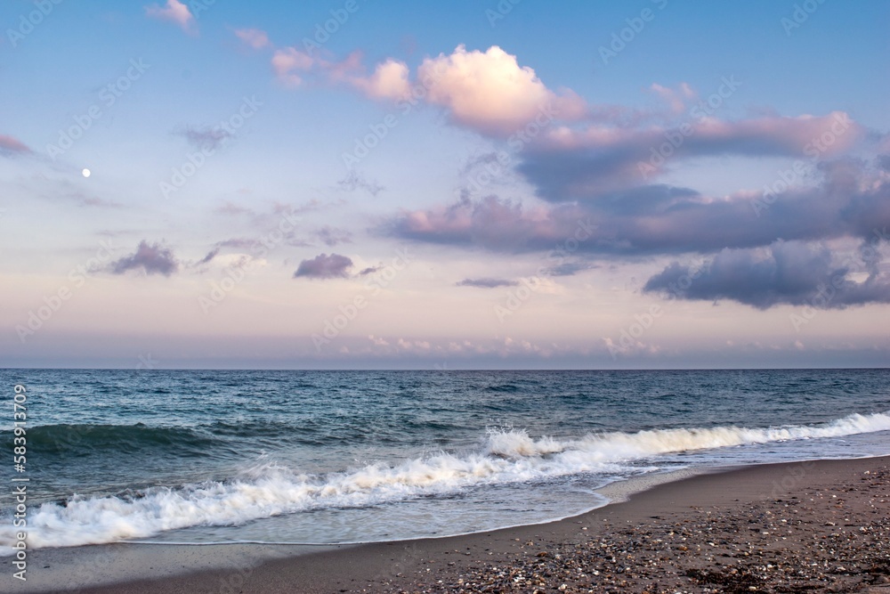 The beach stretches endlessly along the shore, a pristine oasis of sand and sea that meets the horizon where billowing clouds float like cotton candy against the brilliant blue sky.