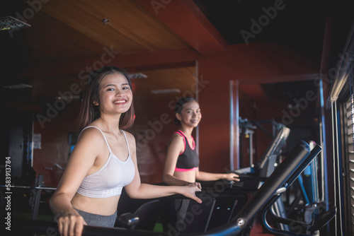 Two pretty asian women smiling while brisk walking on the treadmill. Working out or doing cardio inside the gym.