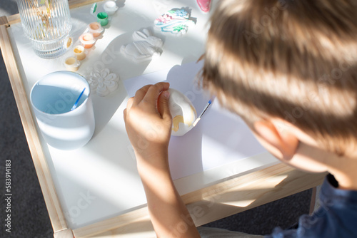 A boy is sitting at a table and decorating an Easter egg. The concept of Easter children's crafts. 