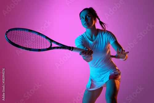Portrait of young female tennis player in uniform with tennis racket training against pink studio background in neon light. Concept of professional sport, movement, health, action. Ad © master1305