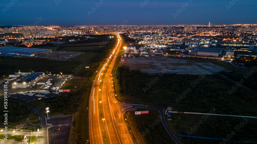 Aerial above view of the bigger highway with big traffic next to forest and the historical and at same time modern city of St. Petersburg at  summer night