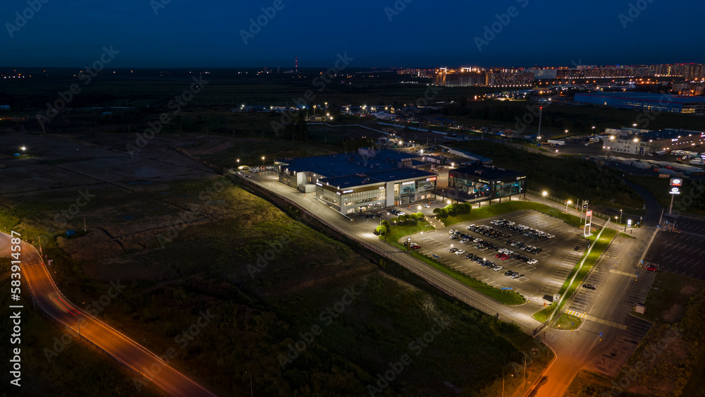 Aerial view of the shops next to bigger highway with many cars and forest in the historical and at same time modern city of St. Petersburg at summer night