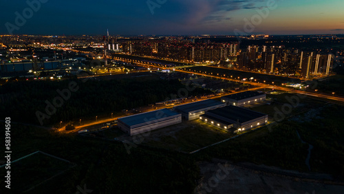 Aerial view of the residential high-rise buildings next to bigger highway with many cars and forest in the historical and at same time modern city of St. Petersburg at light summer night