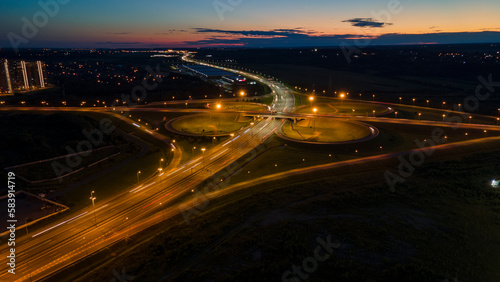 Aerial view of the bigger traffic interchange with many cars next to forest and the historical and at same time modern city of St. Petersburg at light night