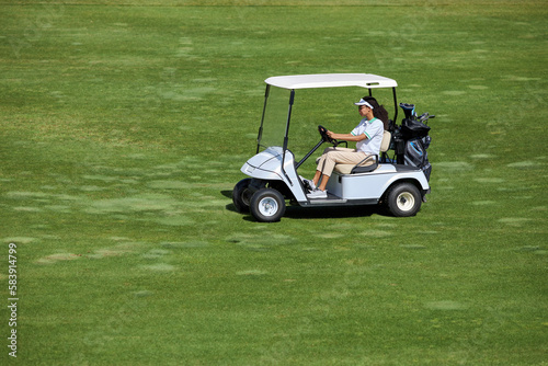High angle view at young woman driving golf cart on green field in sunlight, copy space