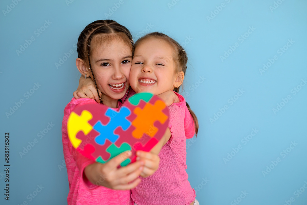 Funny laughable girls show a heart- shaped postcard with pieces of multicolored puzzles . Heart in Viva Magenta color for children with autism