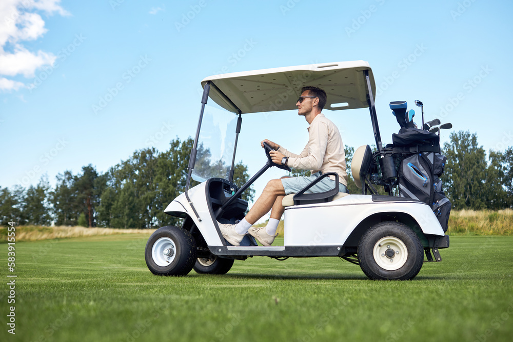 Full length side view of man driving golf cart across green field in sports club, copy space Full length side view of man driving golf cart across green field in sports club, copy space