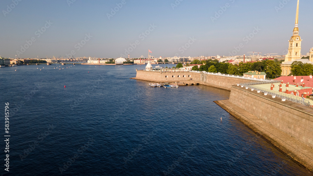 Aerial parallel along view of wall of the Peter-Pavel's Fortress, Church next to the river and water channel in the historical centre of city of St. Petersburg at clear summer sunrise, camera up