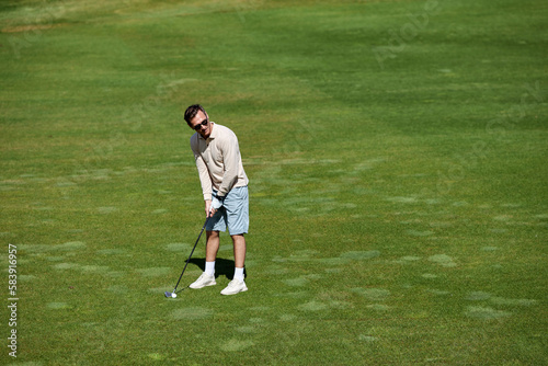 High angle portrait of rich sporty man playing golf on green field in sunlight, copy space