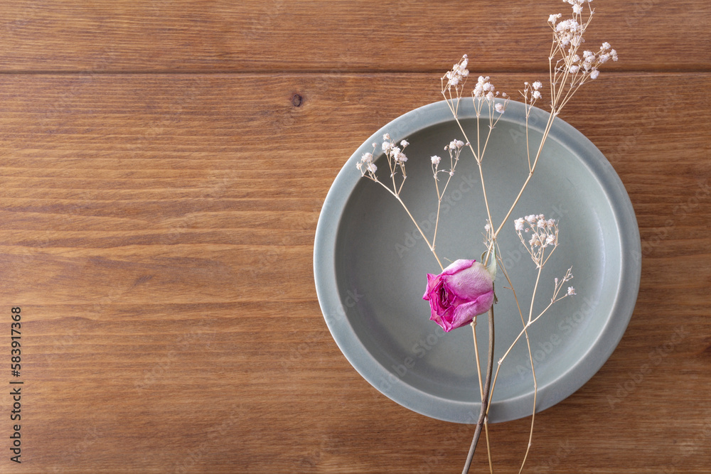 Dried pink roses on a khaki round plate on a wooden table
