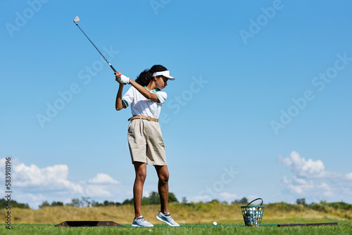 Side view portrait of sporty woman playing golf on green grass outdoors and swinging golf club, copy space