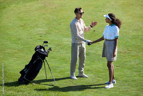Full length portrait of two golf players shaking hands on green field after enjoying game match